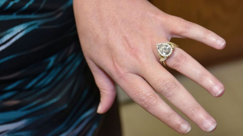 A close-up of a woman's hand wearing a large, pear-shaped diamond ring with a gold band and diamond halo.