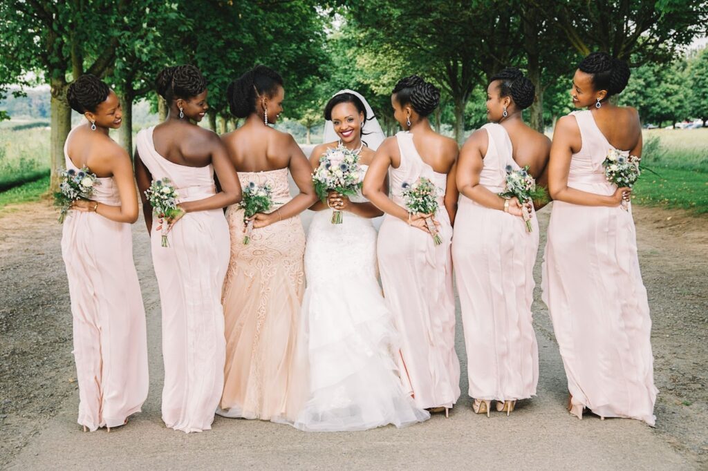Bride and bridesmaid share a joyful moment, holding colorful floral bouquets with smiles, dressed elegantly in white and teal gowns.
