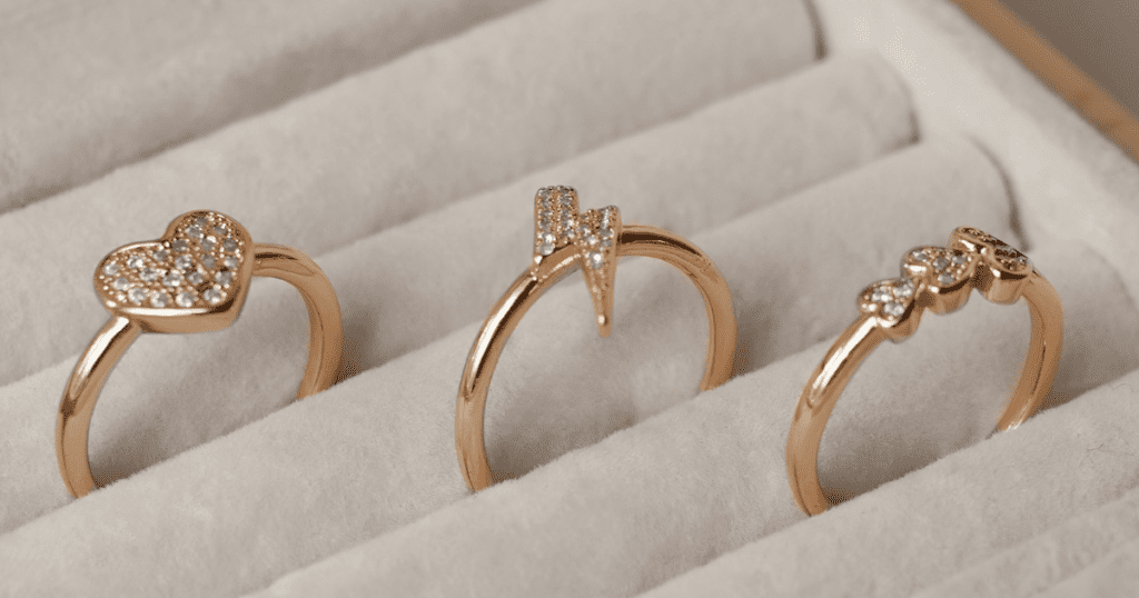 Three delicate rose gold rings: a heart-shaped with diamonds, a lightning bolt design, and a trio of teardrop diamonds, displayed in a soft velvet case.