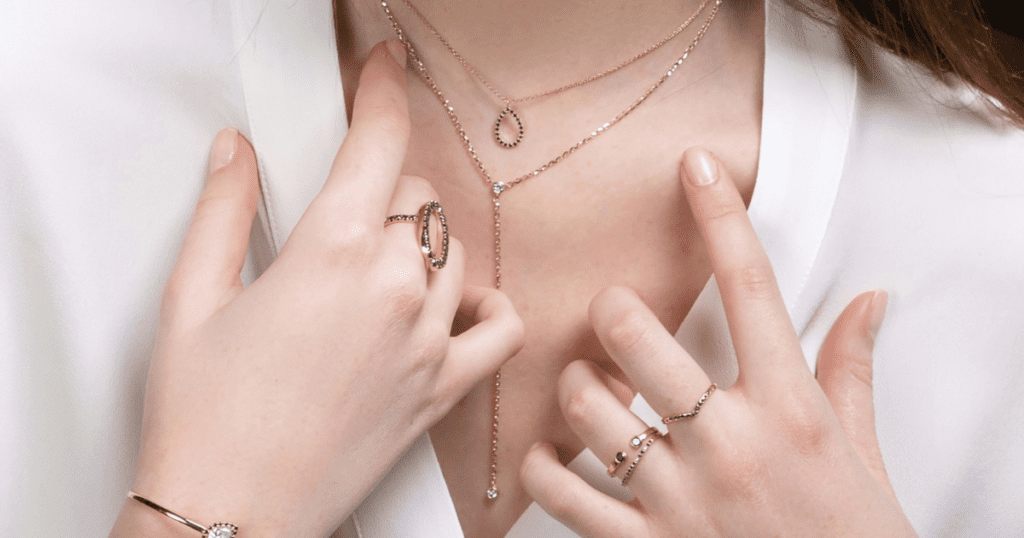 A woman wearing layered gold necklaces and multiple rings, her hands delicately touching her jewelry, highlighting the elegant designs.