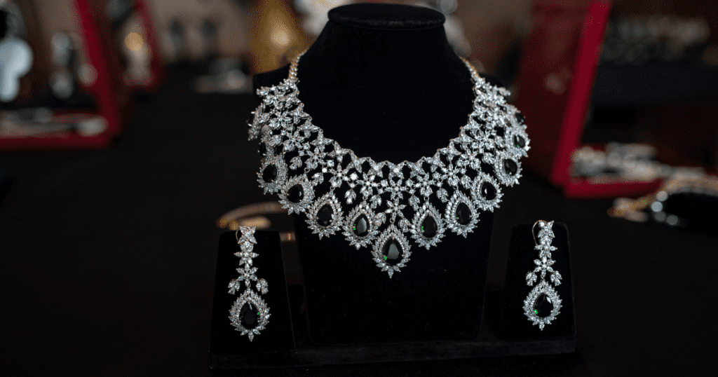 Elegant diamond and green gemstone necklace with matching earrings displayed on a black velvet stand, showcasing intricate design and craftsmanship