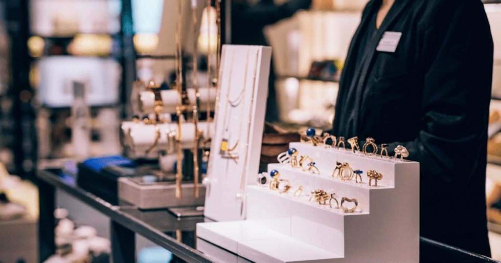 A jewelry display featuring an array of gold and silver rings and necklaces on white stands, with a salesperson in the background, creating a luxurious ambiance.