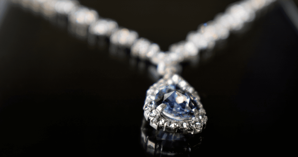 Close-up of a stunning necklace featuring a large, blue teardrop gemstone surrounded by smaller diamonds, elegantly laid on a black surface.