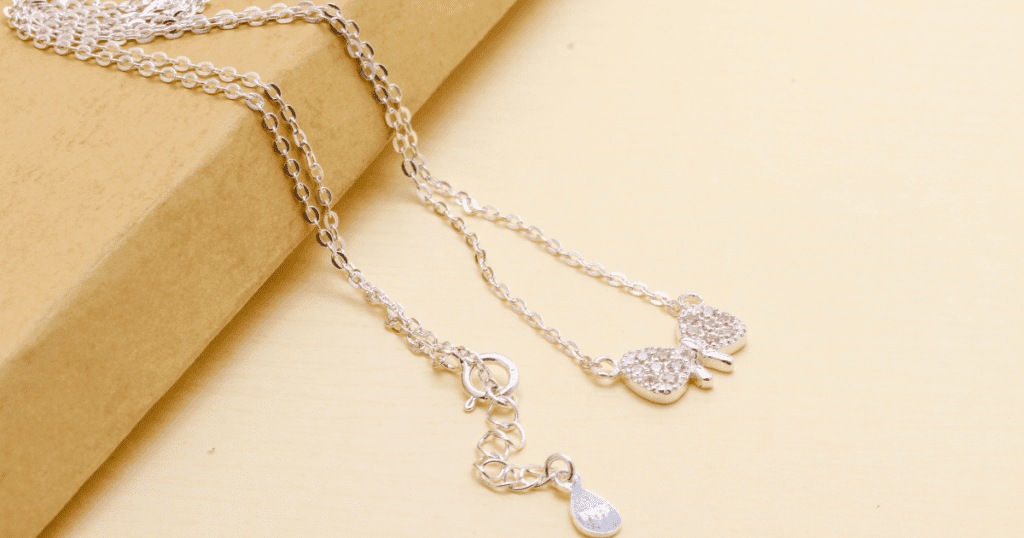 A delicate silver necklace with a butterfly pendant adorned with sparkling stones, elegantly displayed on a soft, beige background.