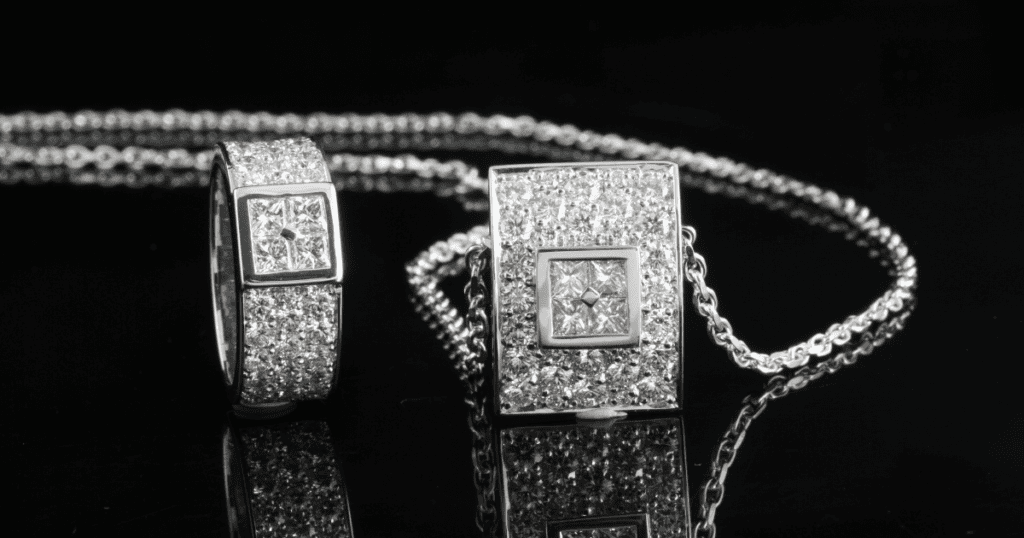 A matching jewelry set featuring a diamond-studded ring and a rectangular pendant on a chain, both with intricate square central designs.