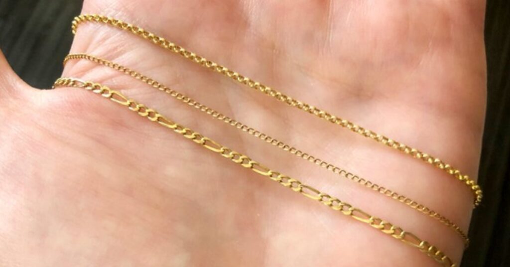 A close-up of a hand displaying three delicate gold chains with varying link patterns, showcasing their intricate design and fine craftsmanship.