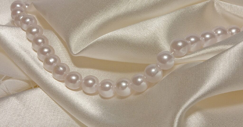 A classic strand of lustrous white pearls elegantly draped over smooth, cream-colored satin fabric, highlighting their timeless beauty and sophistication.