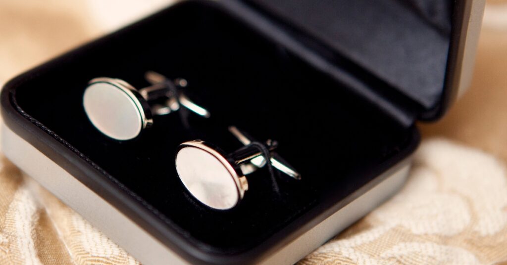 A pair of sleek, round silver cufflinks displayed in an elegant black velvet box, perfect for formal wear, adding a refined touch to any outfit.