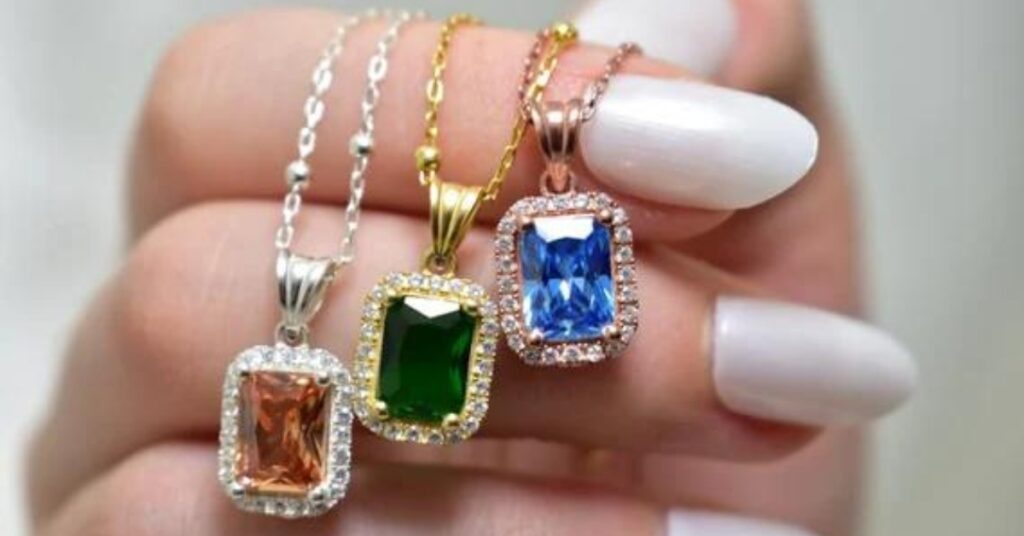 Three radiant gemstone pendants in green, blue, and orange hues set in gold, silver, and rose gold chains, each surrounded by sparkling diamonds.
