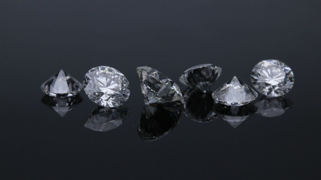 A group of sparkling, faceted diamonds placed on a sleek black surface, each reflecting light in different directions with clarity and brillianc