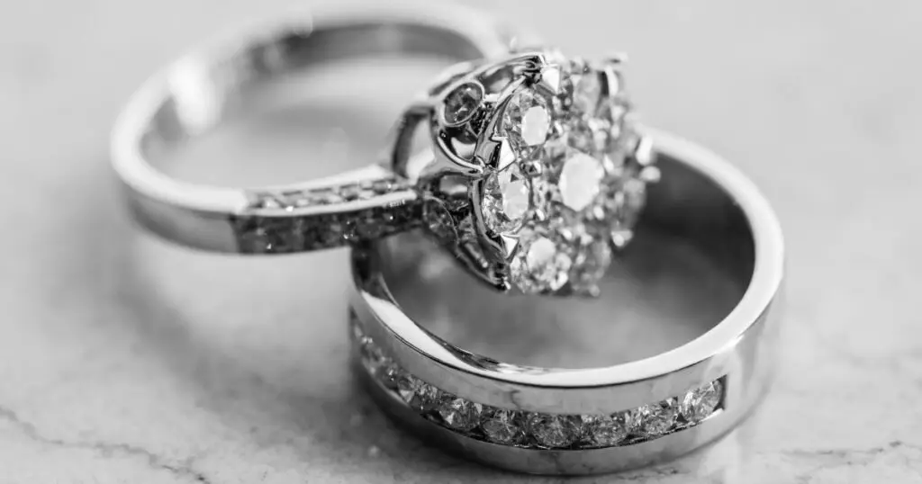 Black and white image of a diamond engagement ring with a floral cluster design, paired with a matching diamond-studded wedding band.