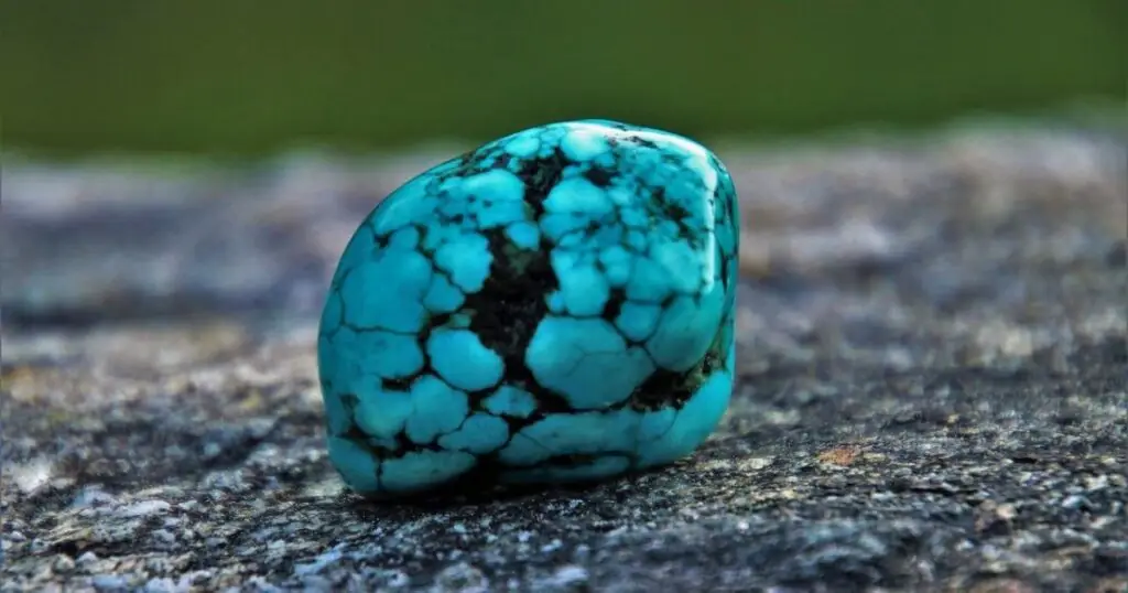 A smooth, turquoise gemstone with a blue-green color and dark matrix inclusions.