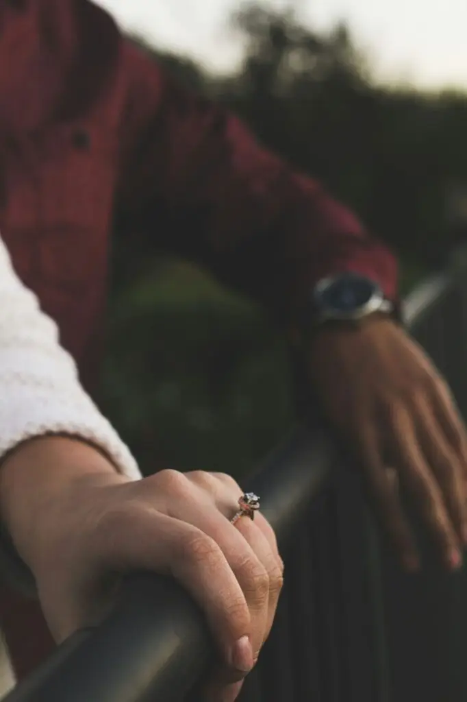 A close-up of a woman's hand wearing a diamond engagement ring, with a man's hand resting beside hers.