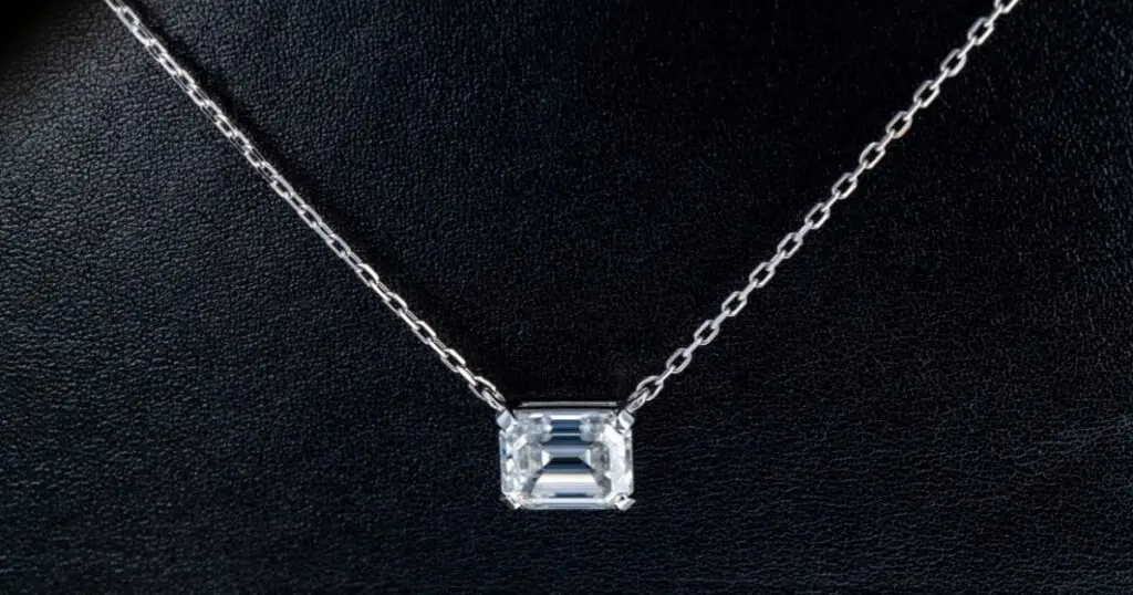  A delicate necklace with a single, emerald-cut diamond pendant. The diamond is set in a simple white gold setting and hangs from a fine chain.