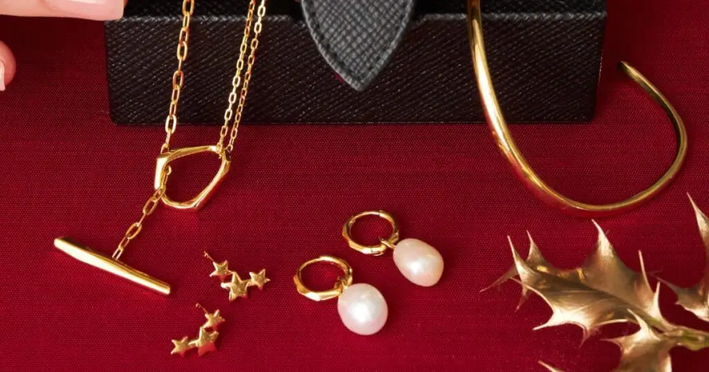 A collection of gold jewelry on a red velvet background. The jewelry includes a necklace, earrings, a bracelet, and a pair of star-shaped studs.