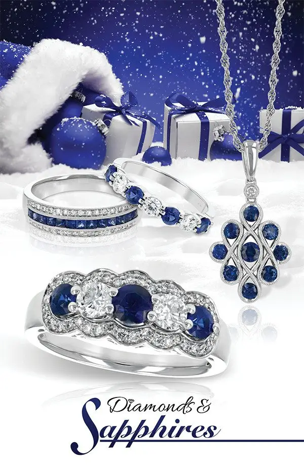 A collection of sapphire and diamond jewelry on a snowy background. The jewelry includes a necklace, earrings, and rings, surrounded by Christmas decorations.