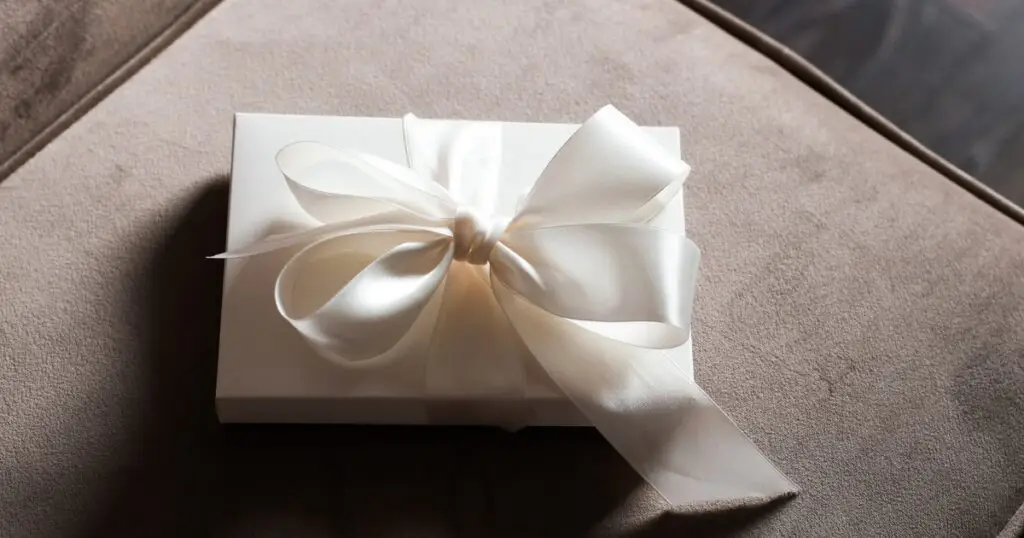 Elegant white gift box with a satin ribbon bow, resting on a soft beige surface, creating a simple yet sophisticated presentation for a special occasion.