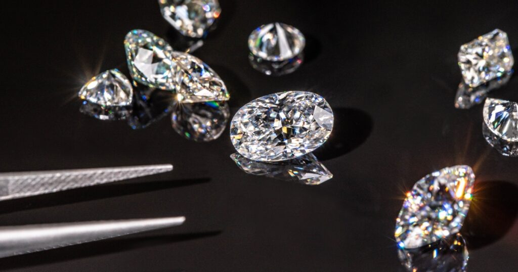 Close-up of dazzling loose diamonds of various cuts and sizes reflecting light on a glossy black surface, with tweezers poised in the foreground.