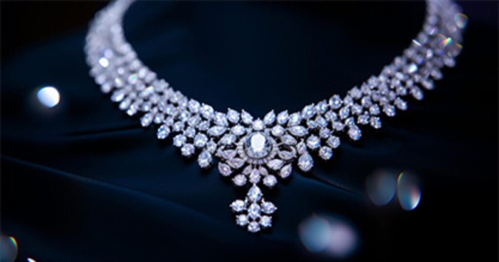 Elegant diamond necklace featuring intricate designs with pear and round-shaped diamonds, resting against a dark fabric background under soft lighting.