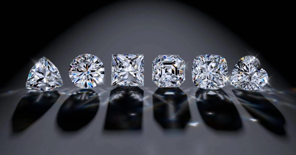 Five diamonds in various cuts—trillion, round, princess, Asscher, cushion, and heart—set on a dark background, casting elegant shadows.