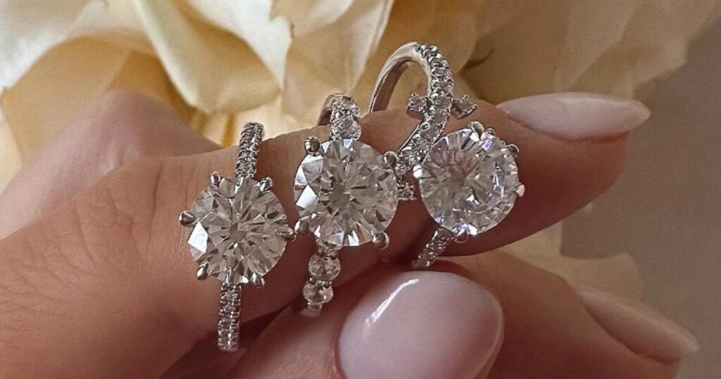 Close-up of three diamond engagement rings with round brilliant-cut diamonds in prong settings on manicured fingers, delicate detailing.