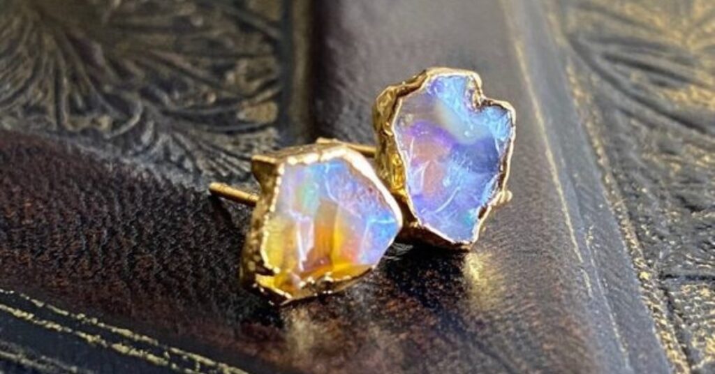 A pair of opal earrings with gold settings, resting on an old book.