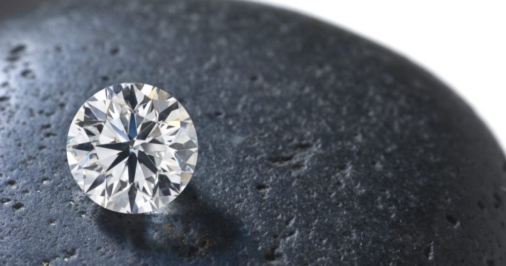 A large, round diamond resting on a smooth, dark stone.