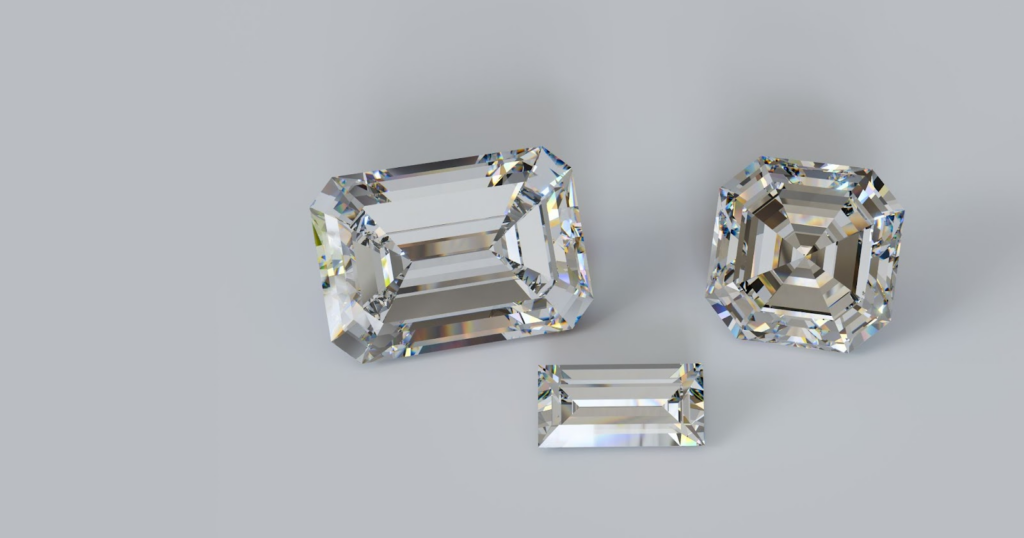 Three emerald-cut diamonds of different sizes on a light gray background.