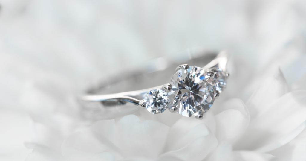 A diamond engagement ring with a cluster of three stones, resting on a bed of white petals.