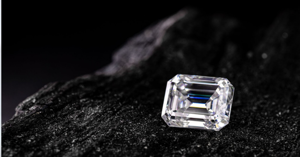 An emerald-cut diamond resting on a dark, textured surface.