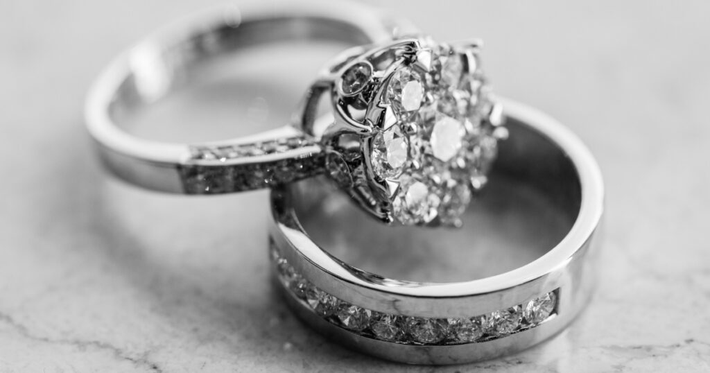 A diamond engagement ring paired with a wedding band, both with intricate diamond detailing, resting on a marble surface.