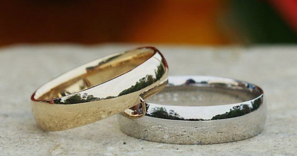 Two wedding bands, one gold and one silver, resting on a stone surface with a blurred background.