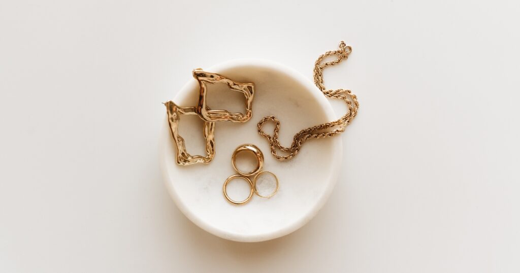 A collection of gold jewelry, including a pair of earrings, a necklace, and rings, displayed on a white marble dish.