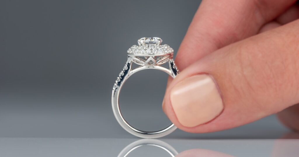 A hand holding a diamond engagement ring with a double halo setting.