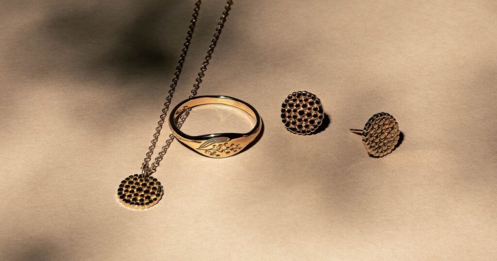 A gold necklace, ring, and earrings with a textured, circular design and a leaf motif on the ring.