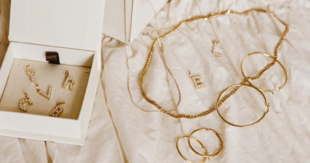 A collection of gold necklaces with letter pendants and hoop earrings, displayed on a white fabric background.