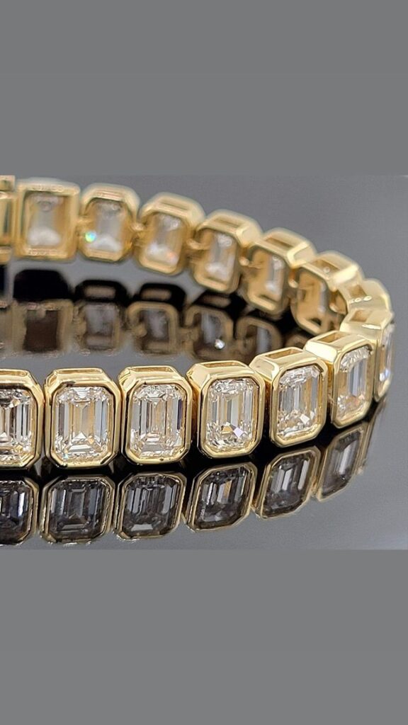 A gold bracelet with a row of emerald-cut diamonds, reflecting on a dark surface.