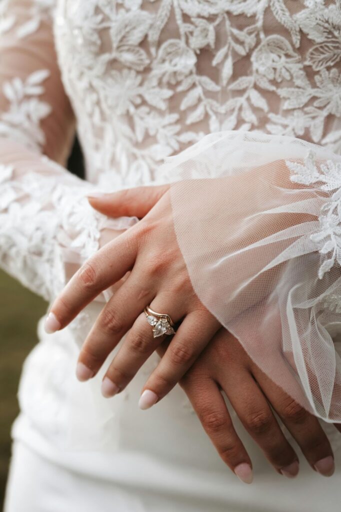 A close-up of a bride's hands showcasing a stunning gold ring with pear-shaped diamonds, complemented by a lace bridal gown.