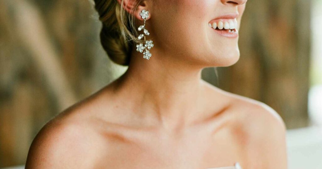 A bride showcasing elegant floral drop earrings with sparkling crystals, perfectly complementing her strapless bridal gown and styled updo.