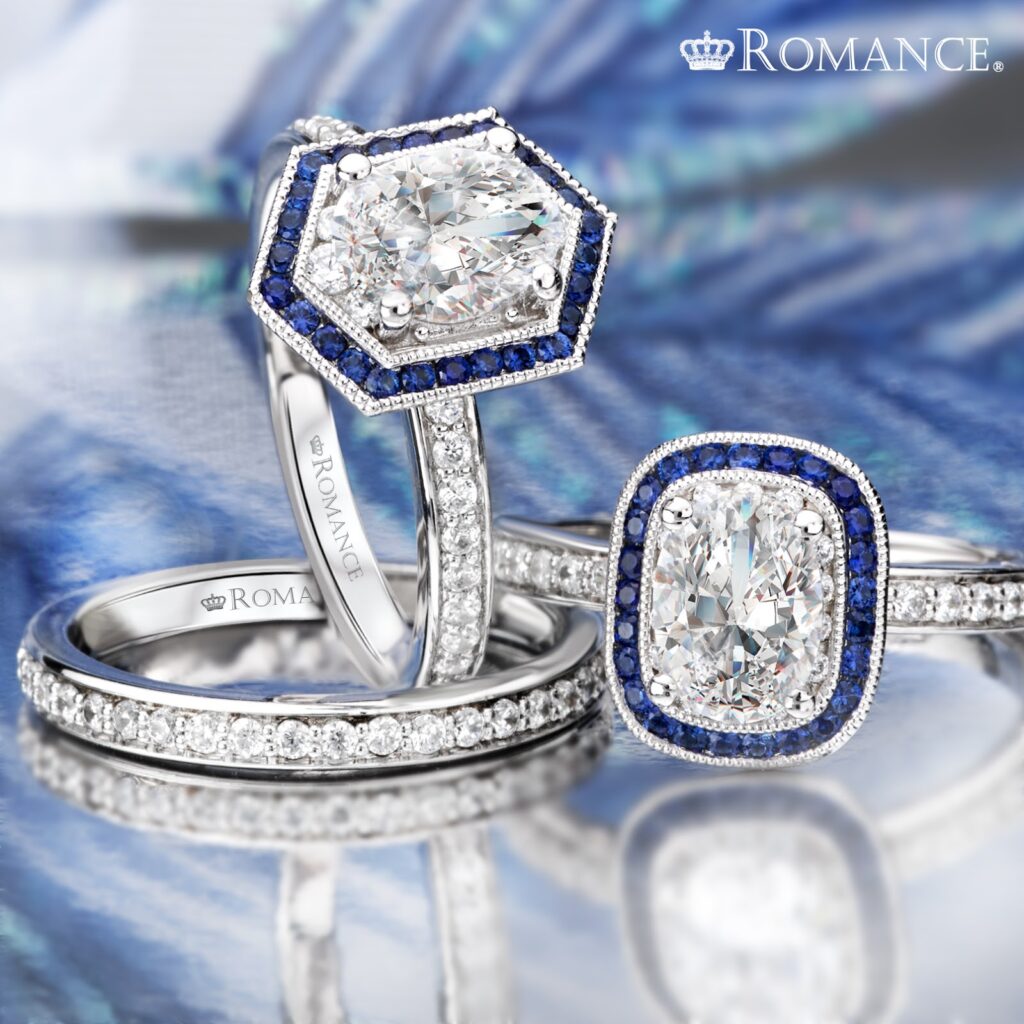 Two diamond engagement rings with blue sapphire accents, one with a hexagonal shape and the other with a cushion-cut center stone, both from Romance.