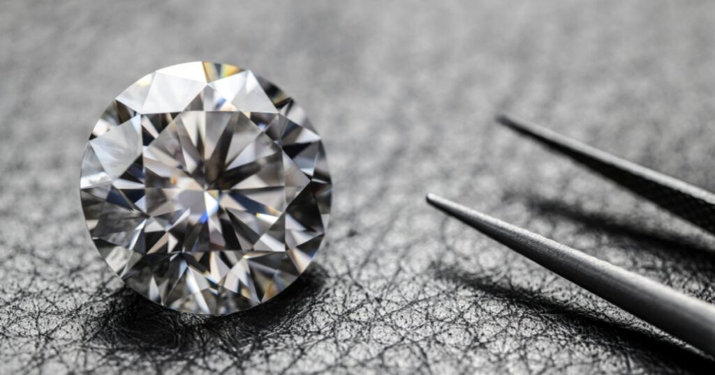 A large, round diamond held in tweezers with a smaller diamond resting on a black surface.