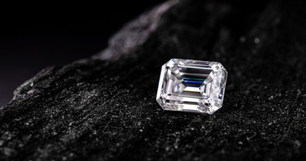 An emerald-cut diamond resting on a dark, textured surface.