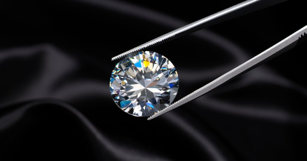 A large, round diamond held in tweezers against a black background.