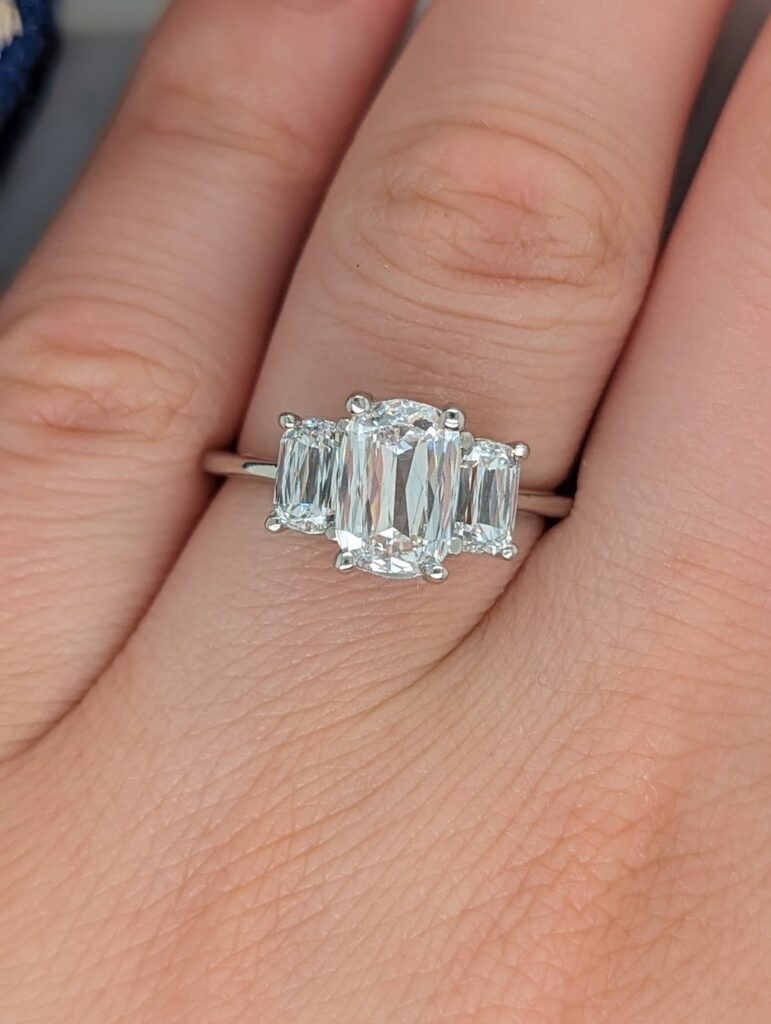 A hand wearing a stunning three-stone engagement ring with emerald-cut diamonds.