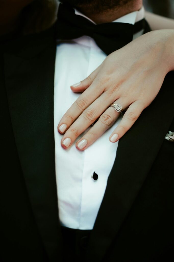 A bride's hand rests gently on her groom's chest, showcasing her engagement ring.