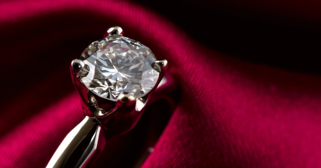 A sparkling diamond engagement ring resting on a rich red velvet background.