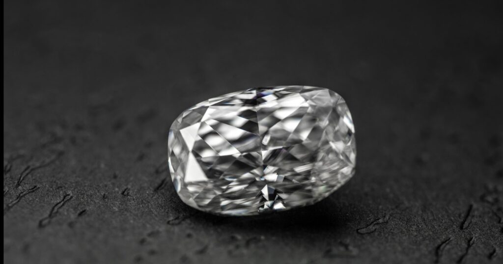 A cushion-cut diamond, showcasing its unique stepped facets and brilliant sparkle, resting on a dark, textured surface.