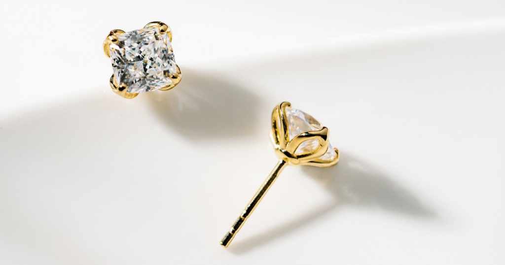 A pair of radiant-cut diamond stud earrings in a gold setting, displayed on a white background.