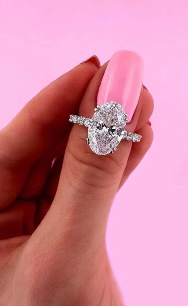 A hand wearing a stunning oval-cut diamond engagement ring with a diamond-studded band.