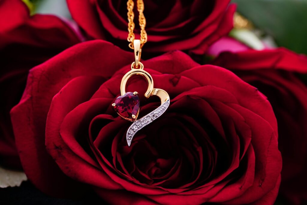 A heart-shaped ruby pendant with diamond accents, nestled within a bed of velvety red roses.